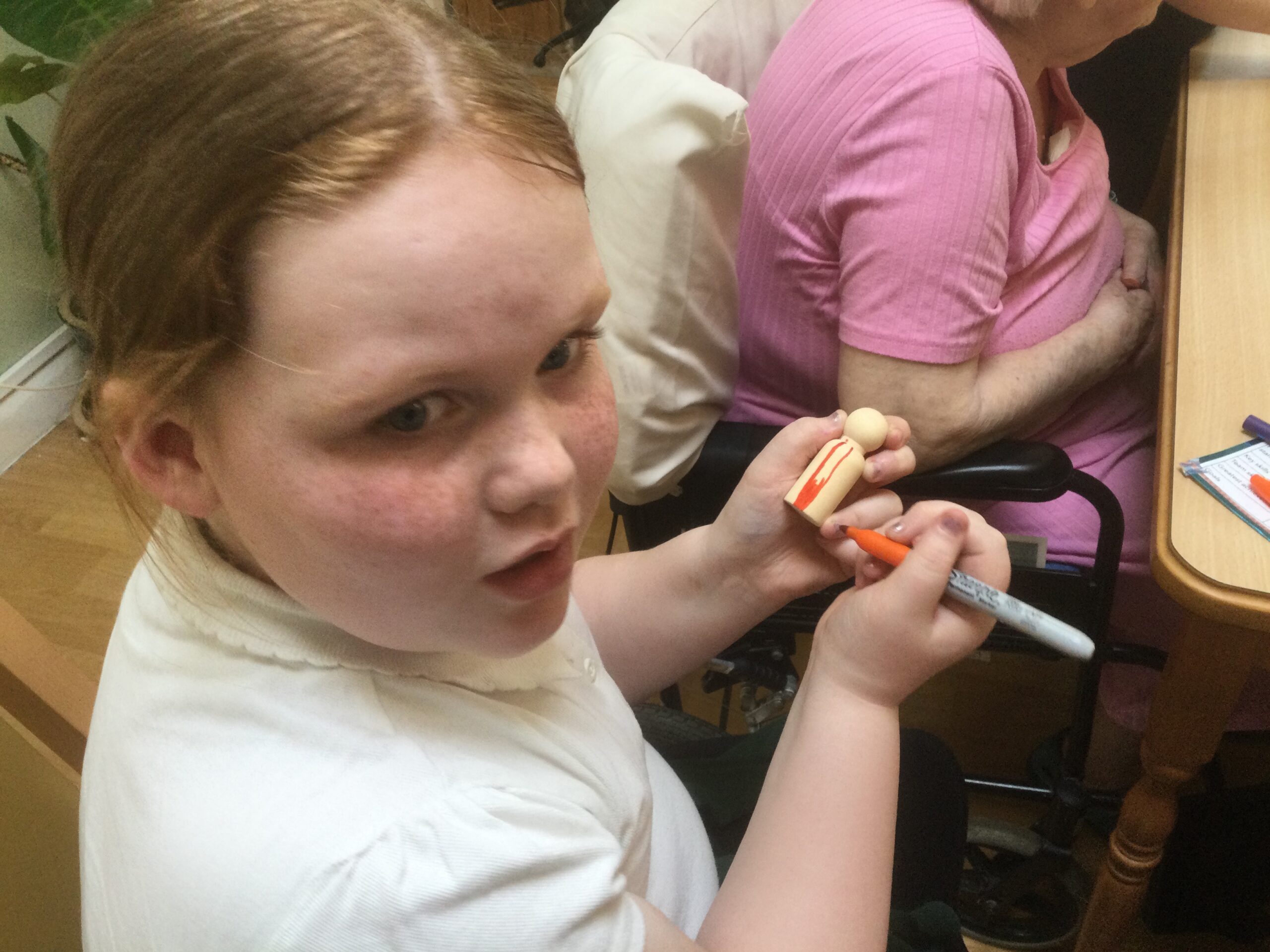 A child grips a wooden figure tightly as she colours it in with orange stripes