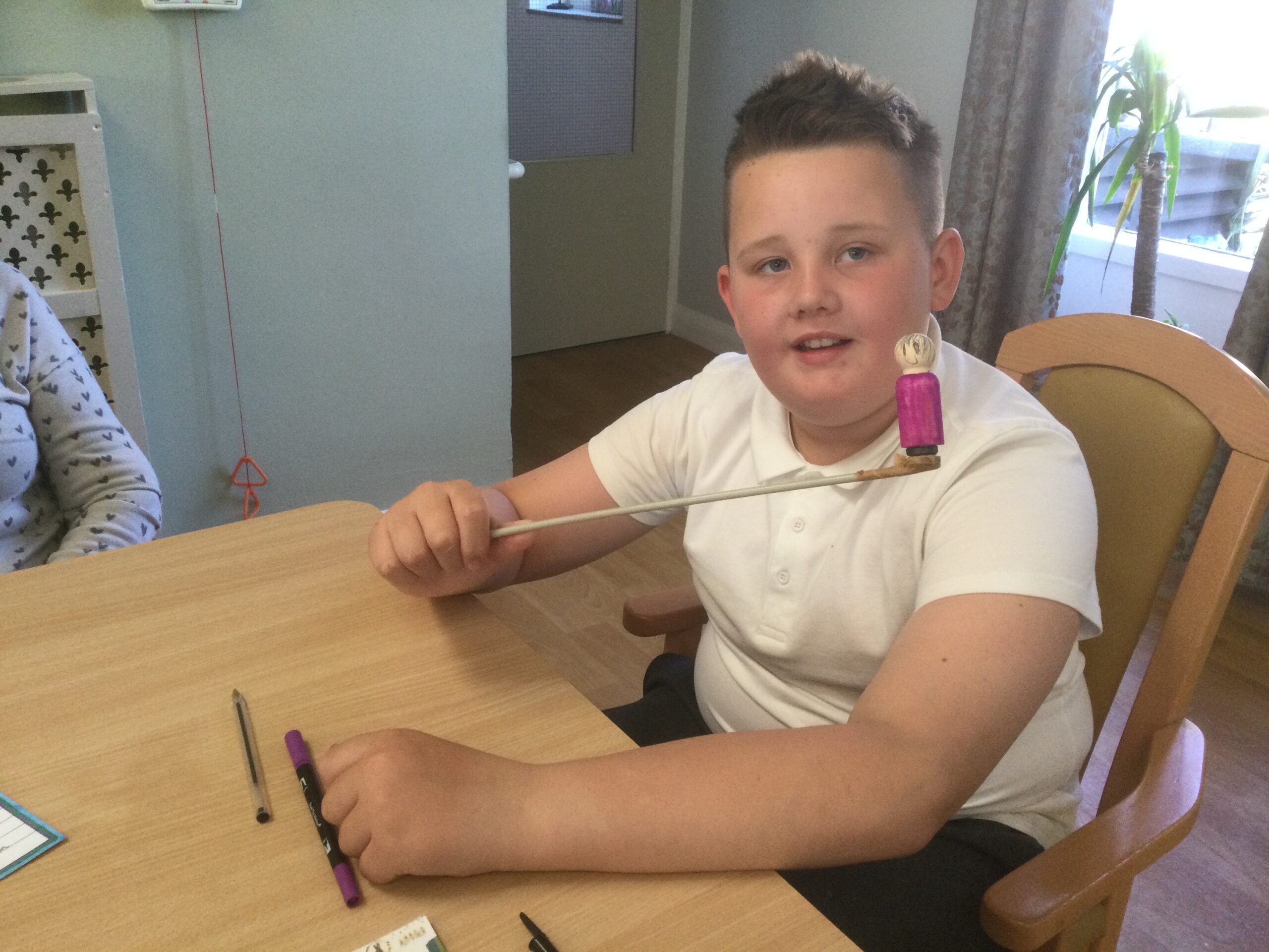 A school boy holds a wooden figure on the end of a long stick