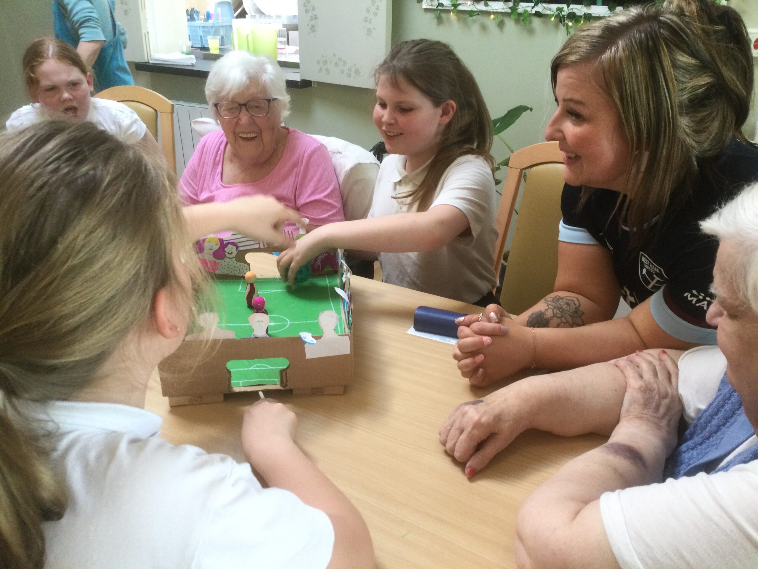 A group of adults and children laughing round a table as they play table top football