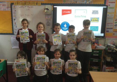 Two rows of school children, each holding a colourful brochure in front of them. Behind them is a screen with the National Lottery Heritage Fund logo clearly visible