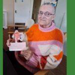 A woman in a colourful pink and orange jumper holds u[ a cardboard football character in similar colours