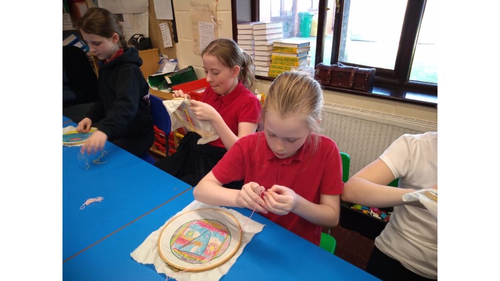 Four girls seated at blue tables each stitching an individual picture
