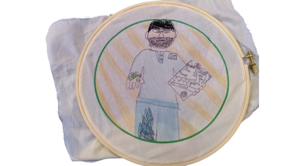A fabric picture of a character holding a copy of The Hooter. His hair has been stitching in in black thread