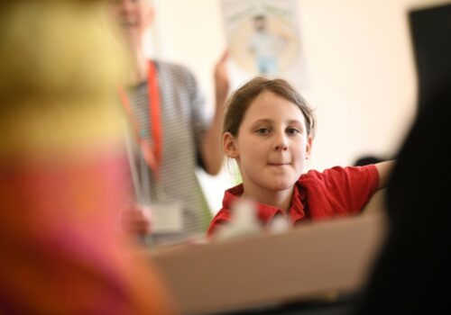 A young girl wearing a red top looks thoughtfully towards the camera