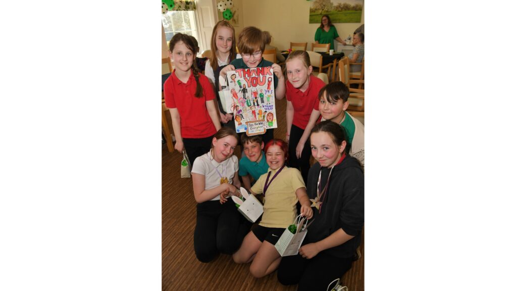 A group of school children holding a large Thank You card, some kneeling on the ground holding party bags