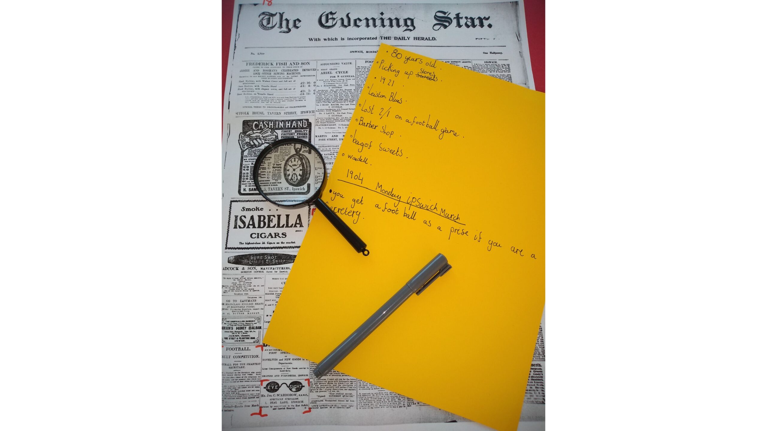 An old copy of the Evening Star newspaper with a magnifying glass, pen and yellow paper for notes lying on top