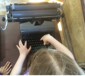 Overhead view of an old fashioned type writer and a child, poking a couple of keys with her fingers