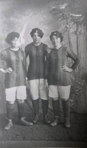 Three female football players pose for a photograph against a studio backdrop