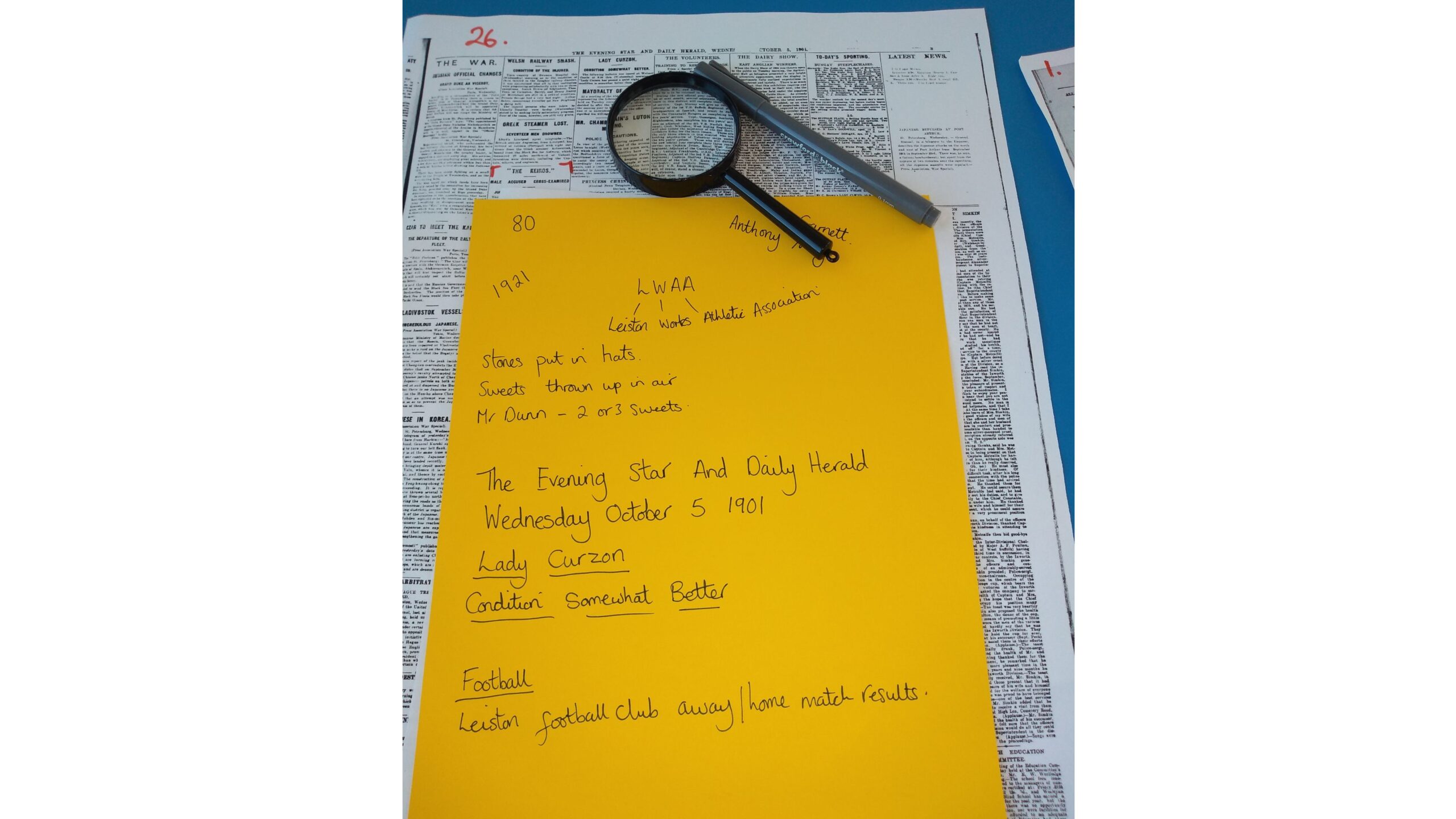 A photocopy of an old newspaper is overlaid with a yellow piece of paper, a magnifying glass and a pen. There are notes jotted down including LWAA Leiston Works Athletic Association and The Evening Star and Daily Heraald Wednesday October 5 1901 Lady Curzon somewhat better