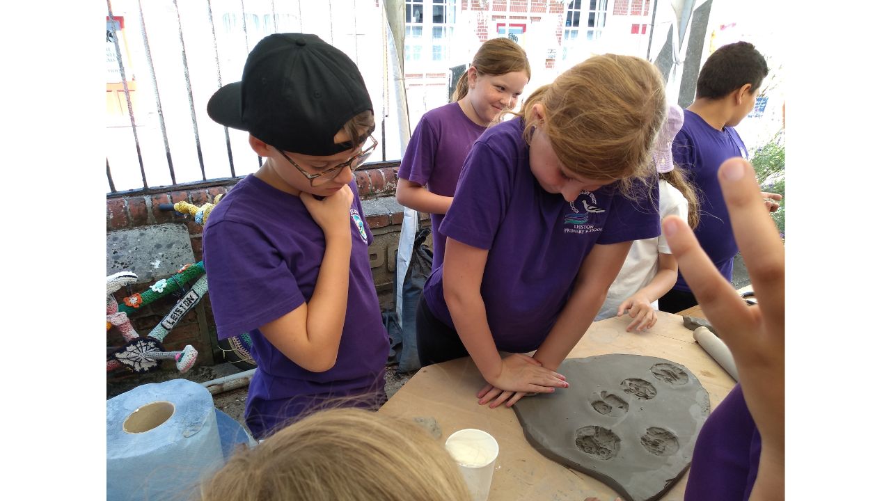Children watch as one child presses into the clay slab in front of her