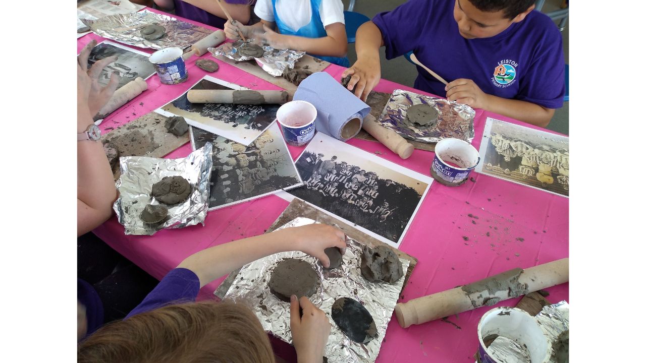 A table covered in clay work materials and photographs with children seated either side