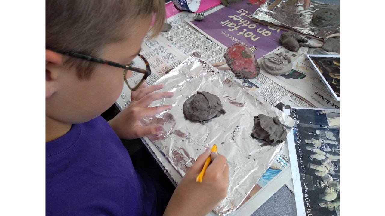 A child uses an implement to add features to his clay face