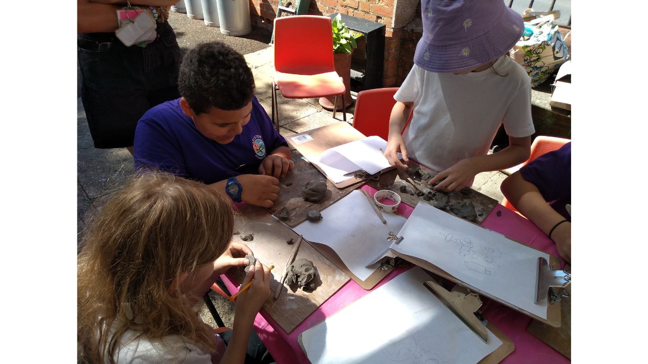 Children gathered around a table with clip boards, clay and cutters in front of them