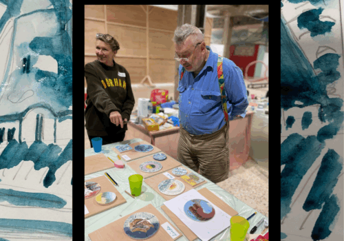 Participant looking at selection of Recharge artworks framed by blue watercolour image of a windmill landscape.