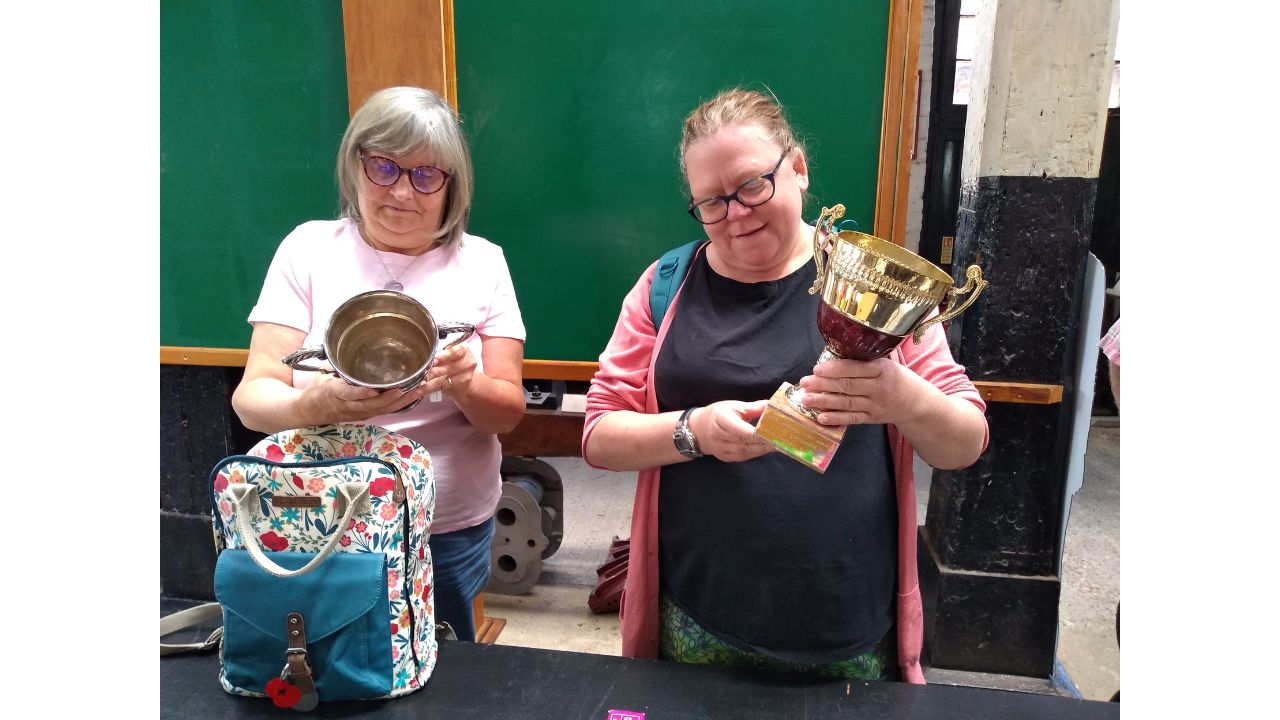 Two adults stand each holding a trophy and looking at it closely