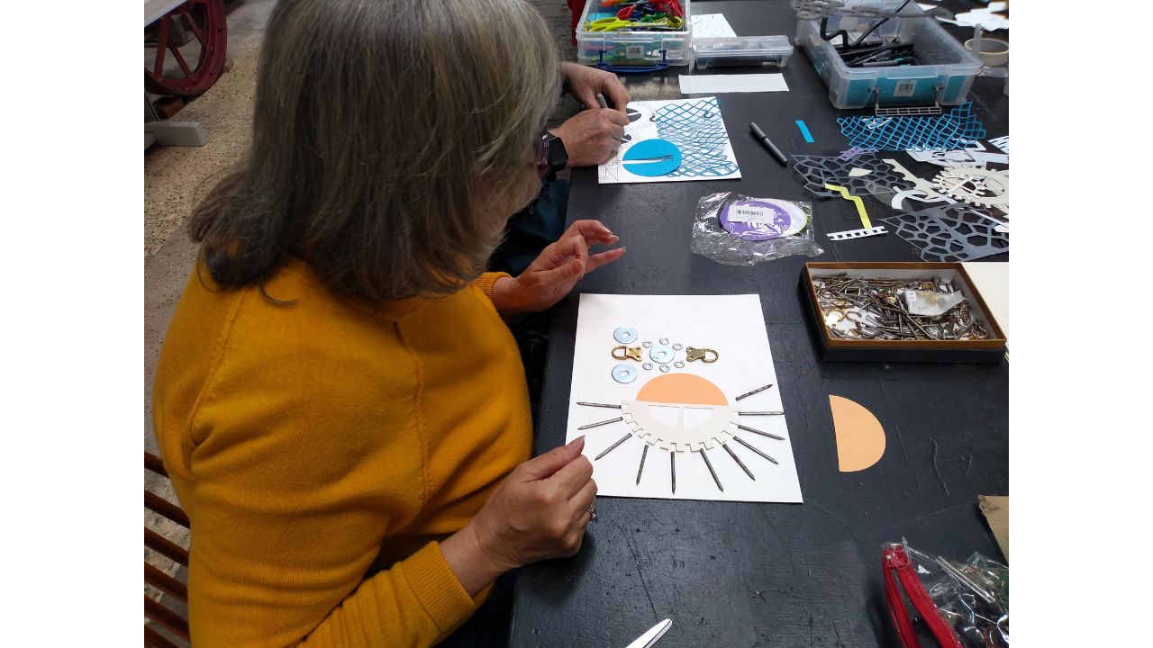 A woman creates a picture using an assortment of objects including nails, washers and cut out objects