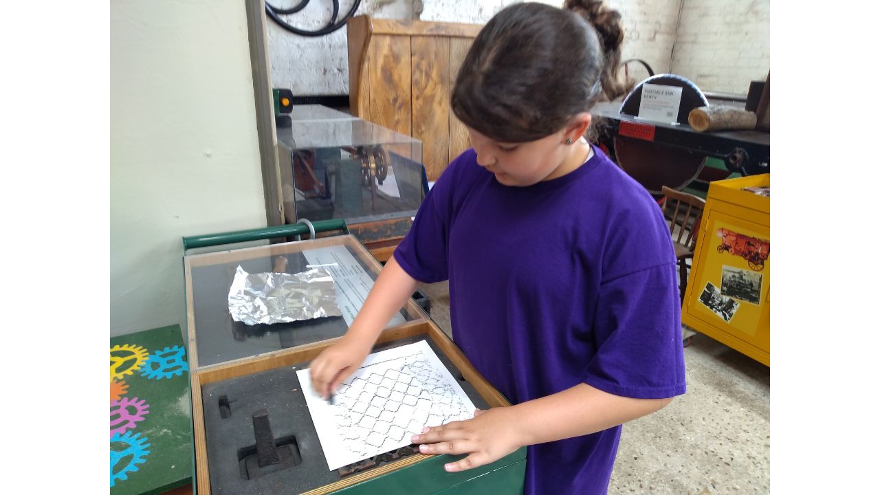 A child takes a pencil rubbing of a piece of iron grating