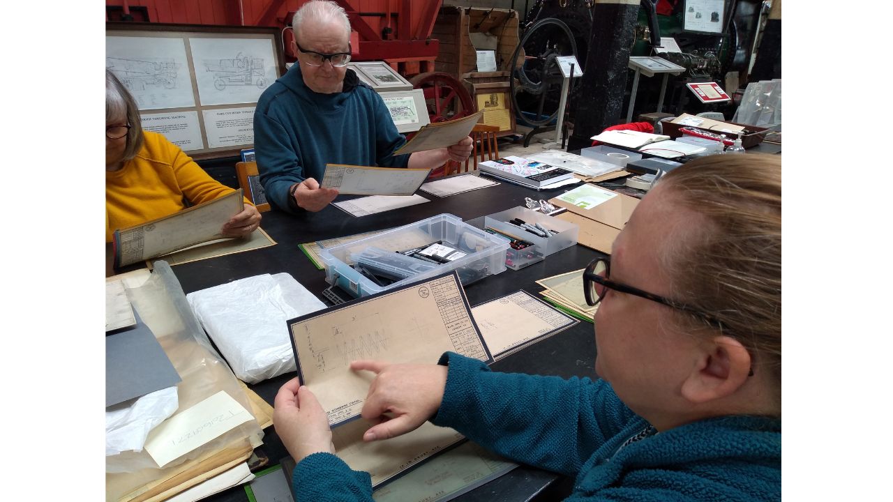 A group of adults examining archive documents - one woman indicates a drawing that looks like a zigzag