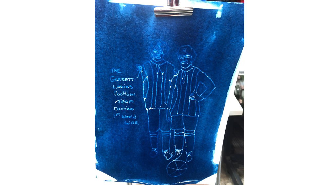 A cyanotype - light sensitive paper with an image of two football players and description The Garrett Ladies Football Team during 1st World War