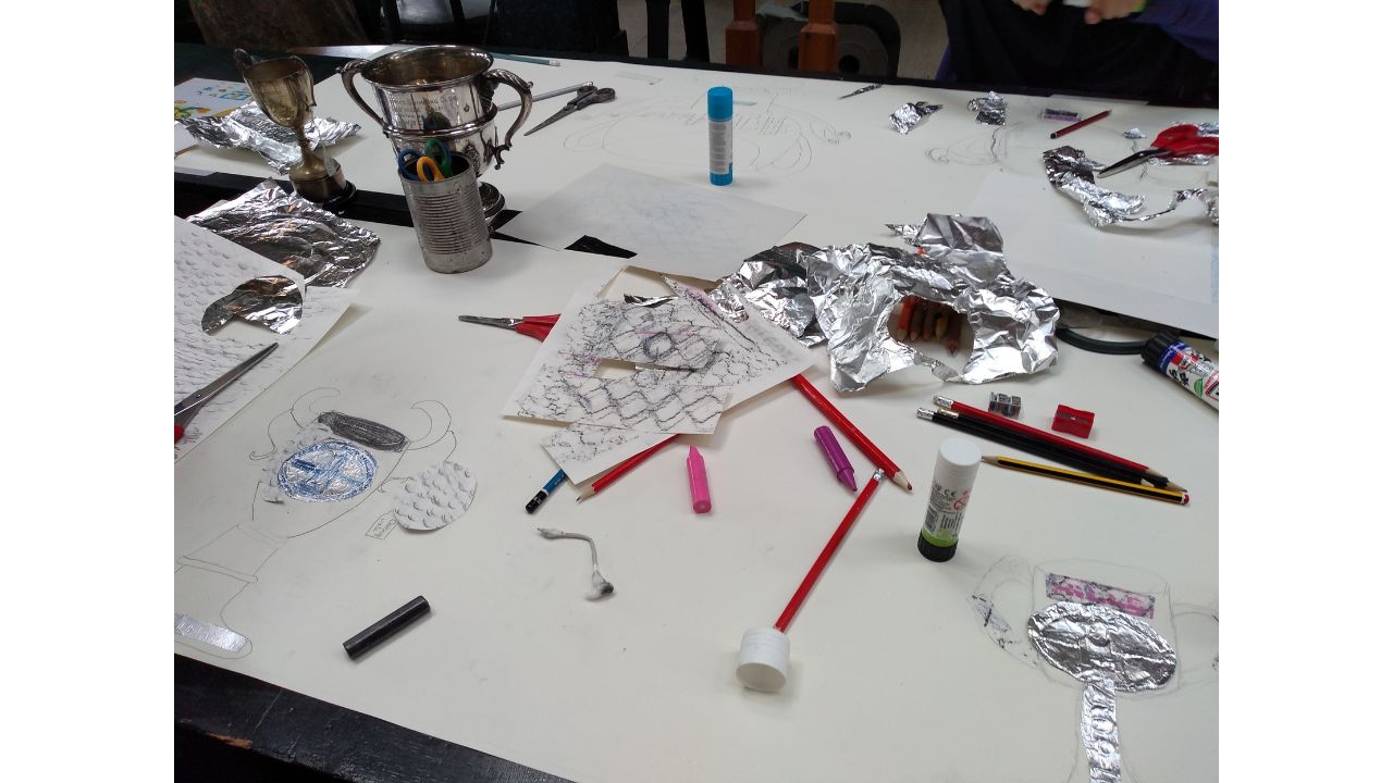 A table top littered with foil, pencils, crayons and a single silver trophy