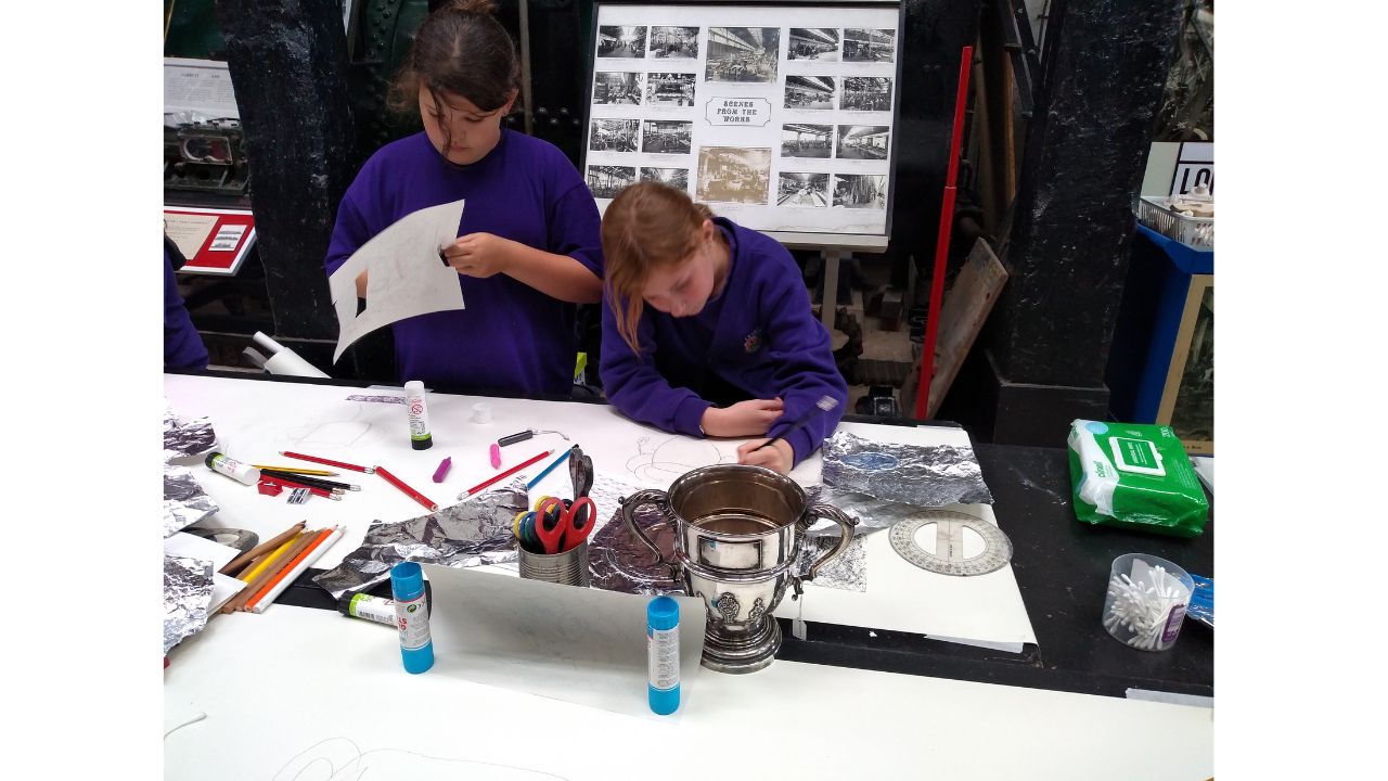 Two school girls drawing and cutting out elements to make their trophies