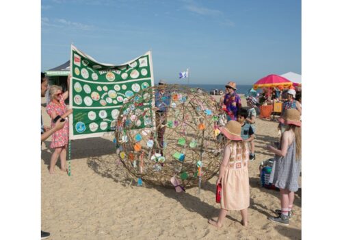 Large banner and willow ball on beach with adults and children looking on