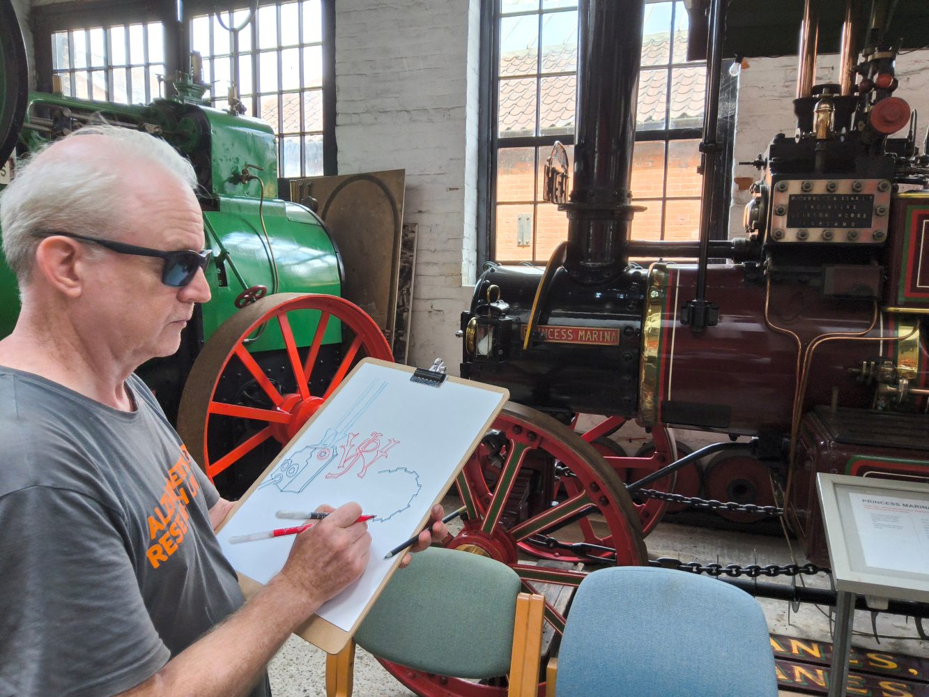A gentleman stands in front of a steam engine, sketching a detail