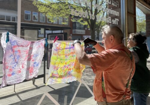 2 participants hanging up decorated cloth in a sunny window