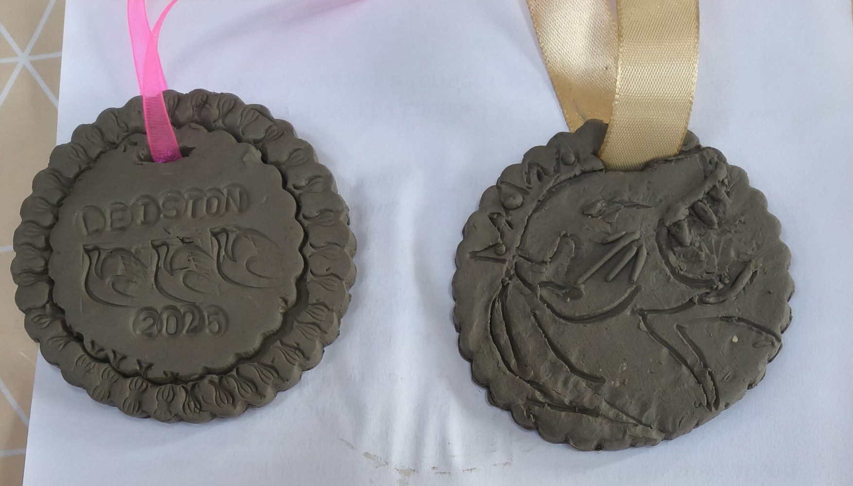 2 clay medals one with the word LEISTON, 3 birds and 2025, the other with a lion's head