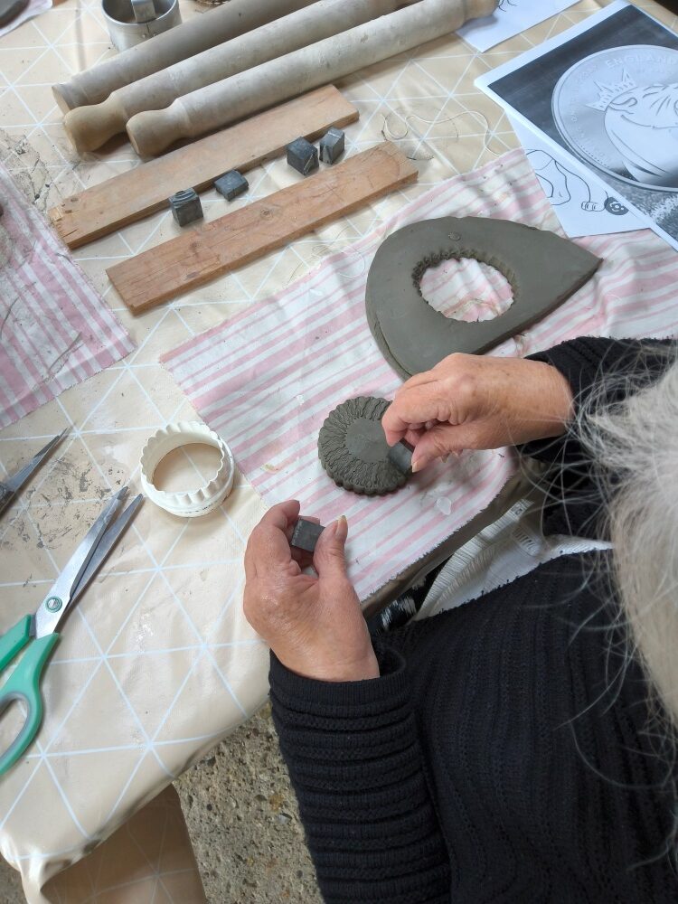 Overhead view of participant cutting out a clay shape and mark making to create pattern