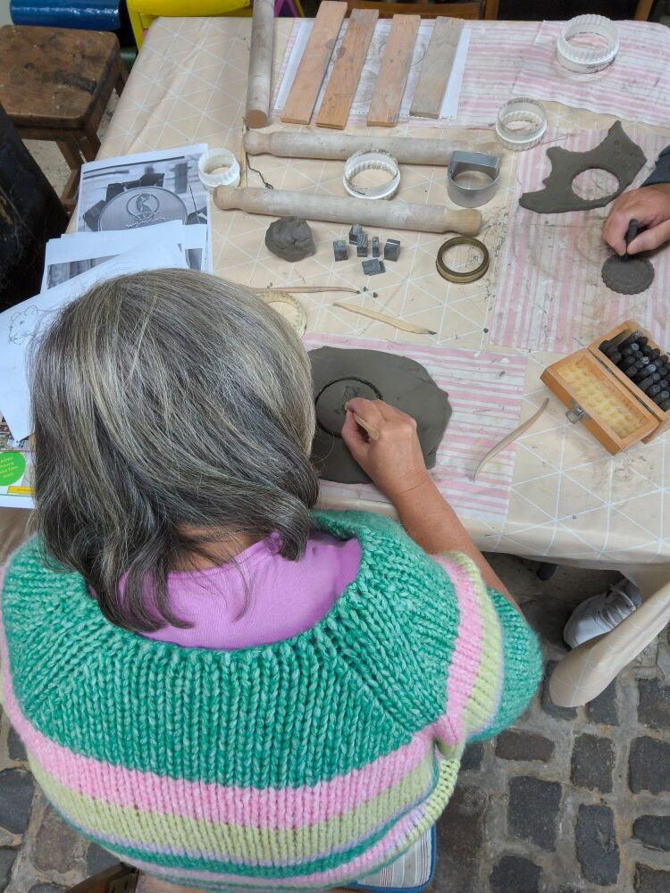 A table covered with tools for working clay, and an individual cutting out a medal