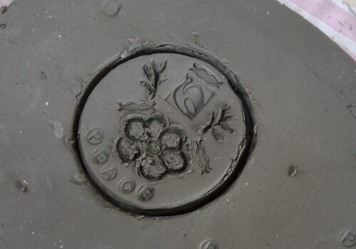 A slab of clay, marked in a circle with the word PEACE under the image of a flower and a bird