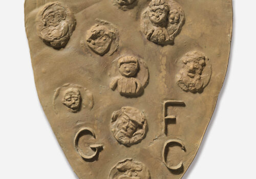 A plaster shield, with 9 individual discs each bearing a different face and the letters GFC