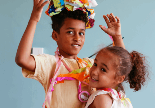 2 kids dressed with one who has a pile of ribbons on their head.
