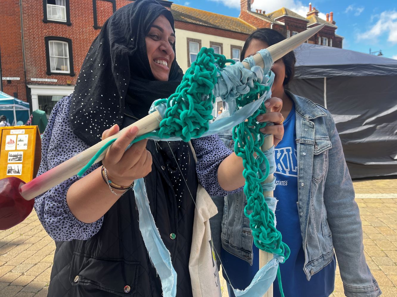 A woman is knitting with very large needles as a second person watches in the background