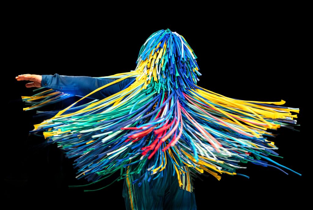 A performer completely covered by ribbons spinning around making them splay out.