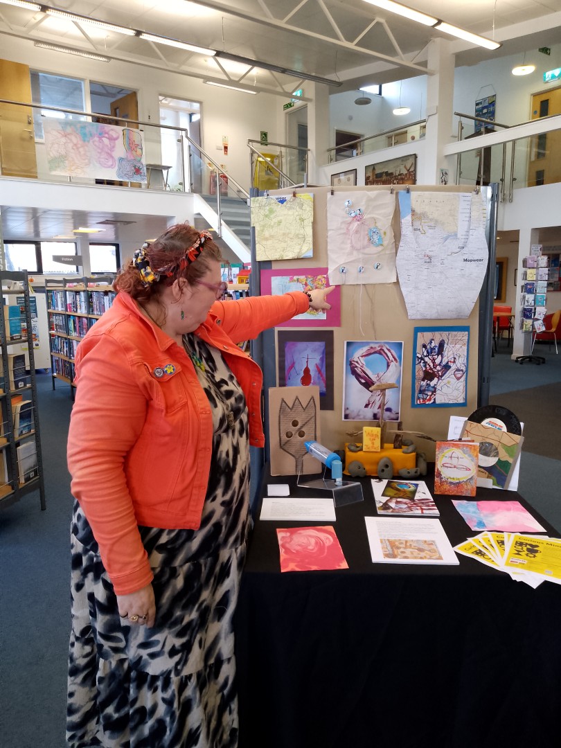 A woman in front of an art display points to her work.