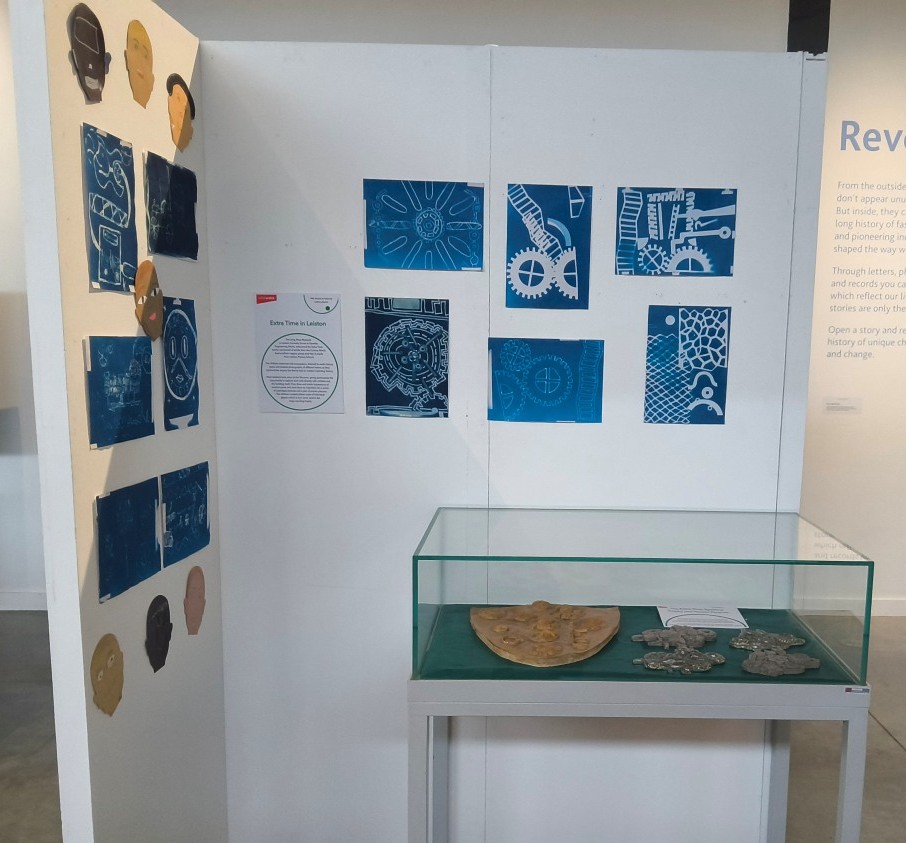 White panels with cyanotypes and paper faces pinned to them and a vitrine in front