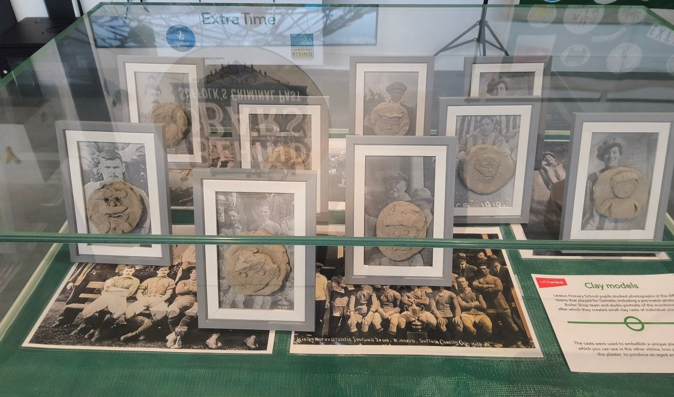 An exhibition display case with old photographs on football teams on top of which stand 9 grey picture frames, each containing a detail from one of the large photograph and a clay model stuck to it