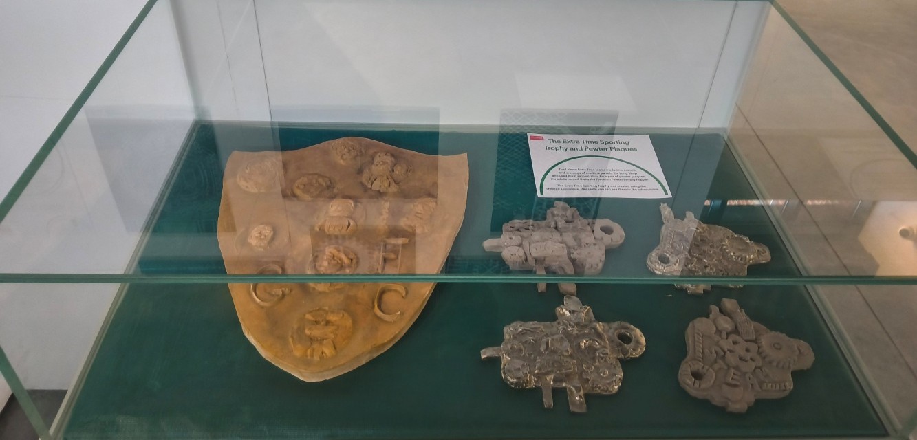 A large plaster sporting shield, two clay models and resulting pewter casts in a display case