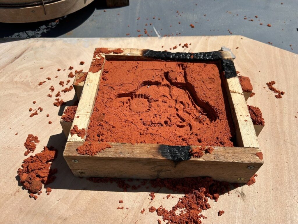 Impression in red sand left by clay model.