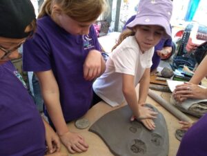 Pupil pressing clay disc into shield