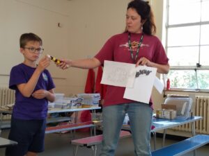 Artist and pupil with an mage, drawing and model of a piece of machinery