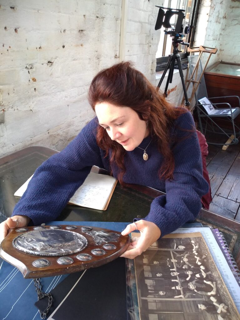 Ellie studies a beautiful sports shield, celebrating inter-Works football matches