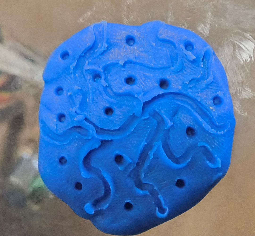 A blue plasticine prototype, marked with swirls and punctured with small holes