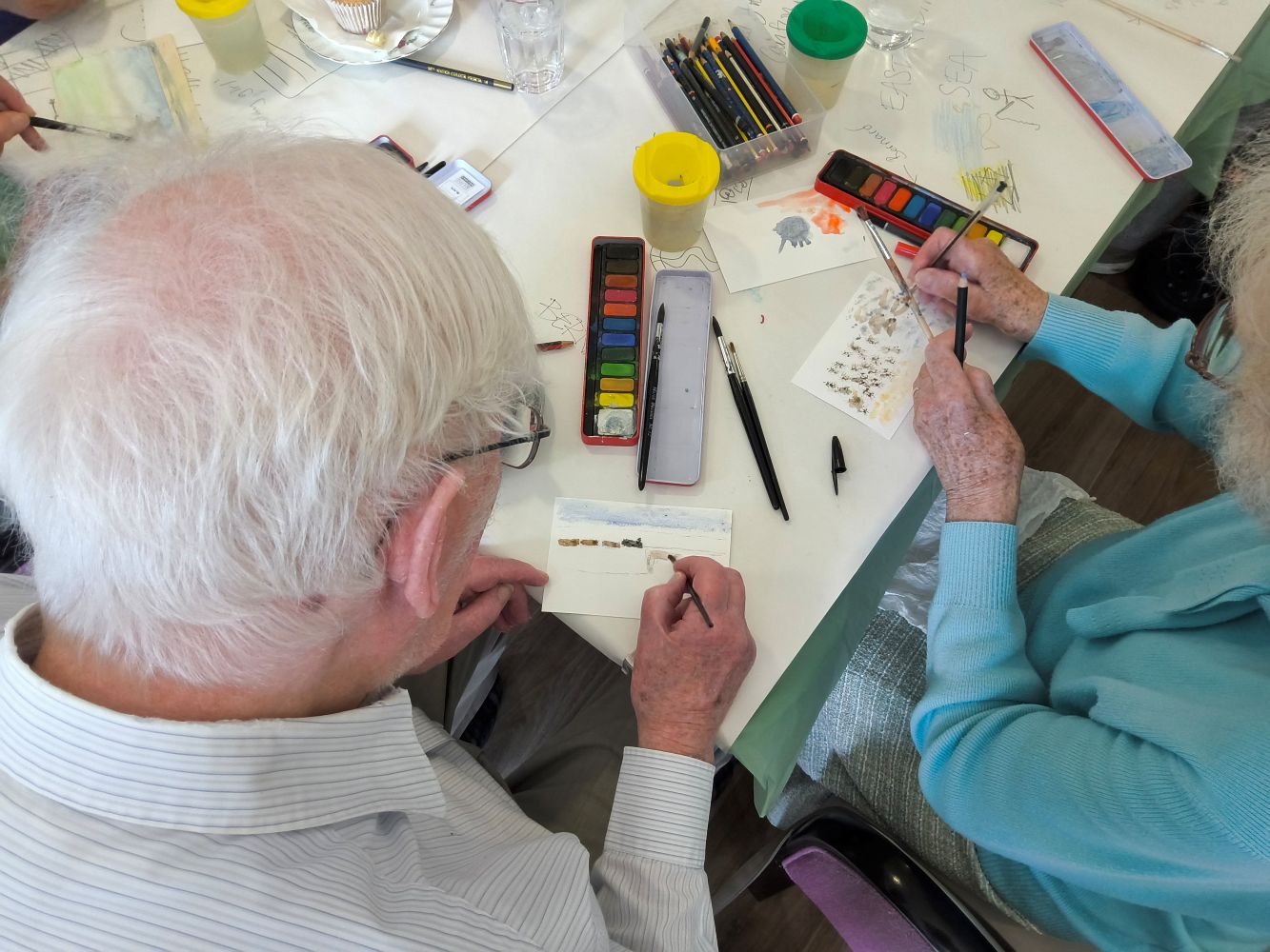 An overhead view of two people painting postcards