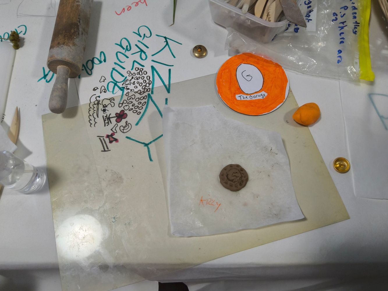 An orange disc with the words The Garage, a clay disc and other art materials