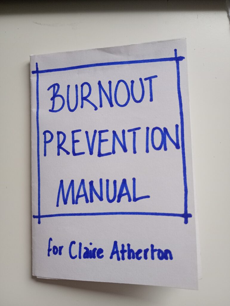 A white piece of paper with the words Burnout Prevention Zine written in blue ink
