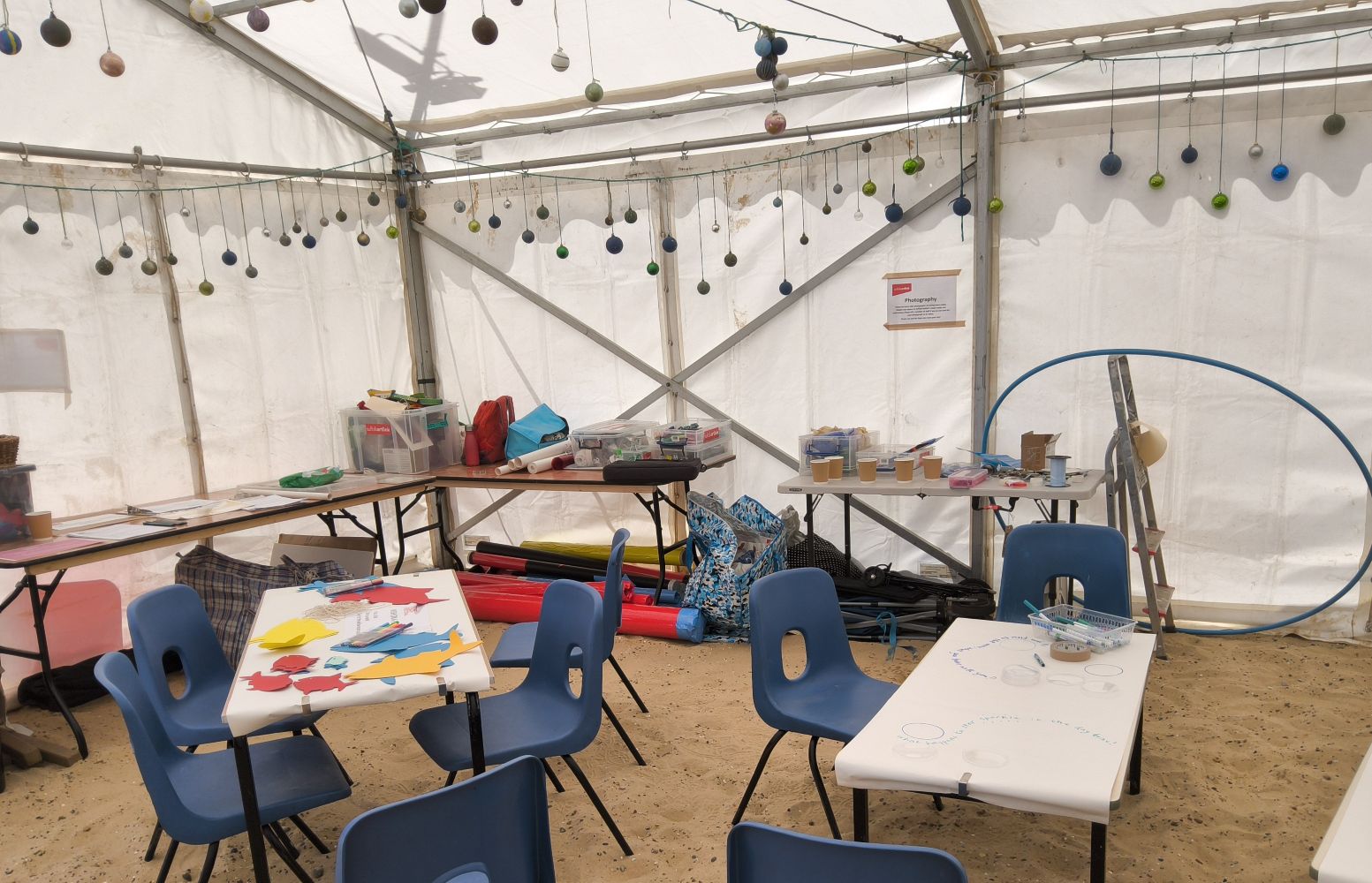 Interior of marquee with baubles suspended along the sides and tables set up with art materials