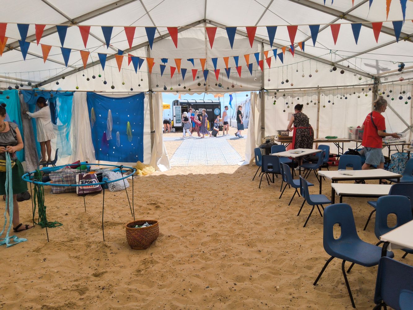 Interior of marquee with bunting, baubles and people setting up tables and hanging coloured fabrics